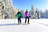 Zwei junge Frauen wandern mit Schneeschuhen durch tief verschneite Winterlandschaft